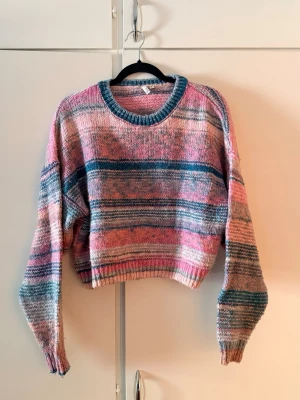 Randig stickad tröja - Säljer en croppad stickad tröja i pastellfärger med ränder i rosa och blått. Tröjan har rund halsringning, långa ärmar och ribbade muddar. Perfekt för dig som gillar en färgglad och avslappnad stil.
