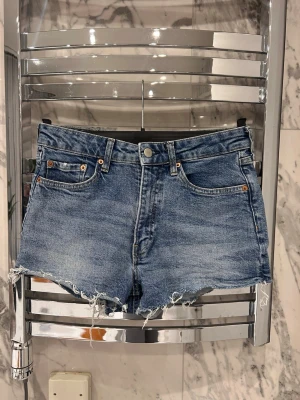 Blå denimshorts  - Snygga blå jeansshorts i storlek 36, från h&m.  Shortsen har knappgylf. Perfekta för sommaren och ger en avslappnad vibe.