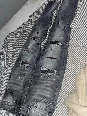 Supply and demand jeans grå  - Säljer ett par grå jeans med slitningar köpte 1 vecka sen och stora hål på framsidan. Jeansen har en tvättad look med färgstänk och skinny fit. Bakfickor och framfickor finns, och materialet är klassisk denim. Perfekta för dig som gillar en edgy streetstil.