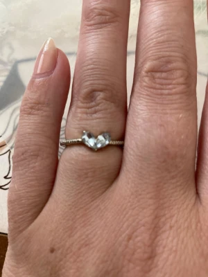 Silverring med hjärtformade stenar - Snygg silverfärgad ring med två hjärtformade, klara stenar framtill. Ringen har en tunn, dekorerad ringskena som ger en elegant look. Perfekt för dig som gillar stilrena och romantiska smycken.