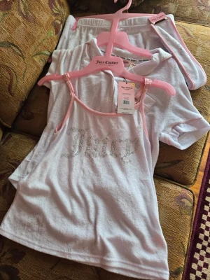 Ljusrosa loungewear-set Juicy Couture - Sött ljusrosa loungewear-set från Juicy Couture med linne och shorts i mjuk frotté. Linnet har tunna axelband och glittrande Juicy-tryck framtill. Shortsen har resår i midjan och matchande detaljer. Perfekt för chill dagar hemma.