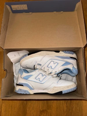 New Balance 550 vita/blå sneakers - Säljer ett par New Balance 550 sneakers i vitt och ljusblått i storlek 42. Skorna har klassisk låg siluett, perforerade detaljer och robust sula. Materialet är mestadels läder med mesh vid plösen. Ikoniskt N på sidan och snygga retrovibbar.