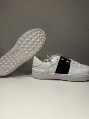 Valentino open sneakers - Snygga vita sneakers från Valentino med en bred mörkblå detalj över sidan och silverfärgade nitar på sulan. Skorna är helt nya i storlek 43 men passar även storlek 42. 