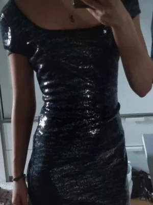 Paljettklänning med tigermönster  - Snygg svart kortklänning från Aftershock med glittrigt material och rundad urringning. Klänningen har korta ärmar och en figurnära passform som ger en cool och festlig look. Perfekt för dig som vill sticka ut med lite extra glitter.