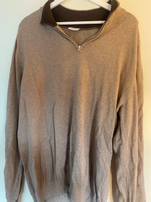 Beige halvzip tröja John Henric XL - Säljer en beige långärmad tröja från John Henric med halvzip och ribbad krage i mörkare ton. Perfekt för dig som gillar stilrena och klassiska plagg. Materialet känns mjukt och bekvämt, och tröjan har ribbade muddar vid ärmslut och nederkant.