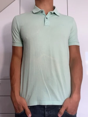Ljusgrön piké från Boss - Ljusgrön piké från Boss. Strl S. Lite missfärgad på framsidan (se bild 1). Modellen är 178 cm och väger 77 kg. Hör gärna av dig vid frågor!