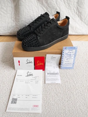 Svarta Louboutin sneakers med nitar - Säljer ett par svarta sneakers från Christian Louboutin i mocka med svarta nitar på tån och klassisk röd sula. Skorna har lågt skaft, svarta skosnören och en stilren design som sticker ut med sina detaljer.