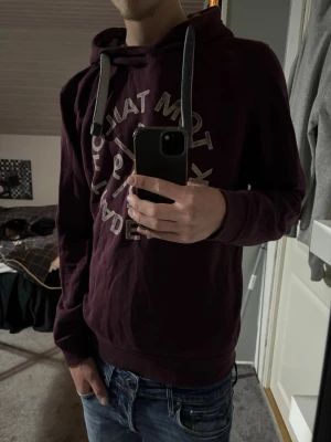 Tom Tailor hoodie - Snygg vinröd hoodie från Tom Tailor med stort tryck framtill och gråa dragsnören i huvan. Mjuk insida och ribbade muddar vid ärmslut och nederkant. Perfekt för chill dagar eller när du vill ha en avslappnad stil.