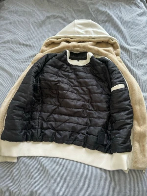 Vit moose knuckles hoodie  - Säljer en vit moose knuckles hoodie med mjukt, fluffigt material och vit huva. Hoodien har dragkedja, två fickor framtill och svart quiltat innerfoder. Snygg detalj med broderad logga på ärmen och ribbade muddar. En silvergrej saknas på loggan (se bild 5). Pälsen går att ta bort. 