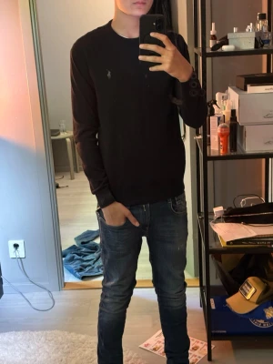 Svart tröja från Polo Ralph Lauren - Klassisk svart långärmad tröja från Polo Ralph Lauren med diskret broderad logga på bröstet. Tröjan har rund halsringning och är tillverkad i mjukt material som sitter snyggt på kroppen. Perfekt till jeans eller chinos.