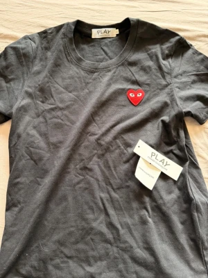 Svart Comme des Garçons PLAY t-shirt - Säljer en svart t-shirt från Comme des Garçons PLAY med det ikoniska röda hjärtat broderat på bröstet. Klassisk rund halsringning och korta ärmar. Tillverkad i mjuk bomull och har en normal passform. Perfekt för en clean och stilren look. Helt ny, prislappen är avtagen men följer med. Priset går att diskutera.