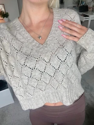 Beige stickad tröja med V-ringning - Beige stickad tröja med V-ringning och ett snyggt hålmönster. Tröjan har långa ärmar och ribbade muddar vid ärmslut och nederkant 💗💗