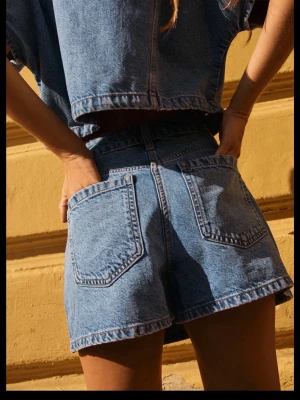 Blå jeansskort med fickor - Snygg jeansskort i klassisk blå denim med hög midja och stora bakfickor. Skorten har en avslappnad passform och synliga sömmar framtill. Perfekt för en cool och avslappnad look