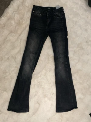 Svarta bootcut jeans från Only - Snygga svarta bootcut jeans från Only med lätt tvättade detaljer och klassisk femficksmodell. Jeansen har hög midja och utsvängda ben, vilket ger en trendig siluett. Perfekta till sneakers eller boots för en cool vardagslook.