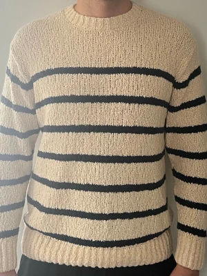 Beige stickad tröja med svarta ränder - Stickad tröja i beige med horisontella svarta ränder. Tröjan har rund halsringning, långa ärmar och ribbstickade muddar vid ärmslut och nederkant. Perfekt för dig som gillar klassisk och avslappnad stil. Helt ny ocj ej använt. Det är storlek L men det är för Medium.