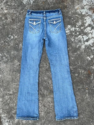 Blå bootcut jeans med detaljer - Snygga blå thriftade yk2 style jeans med coola fickdetaljer bak. Jeansen har en lätt utsvängd passform nertill. ❤️‍🔥❤️‍🔥 sitter jättesnyggt på! Passar mig som är 1,70, går snyggt över skon 