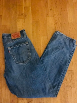 Levi's 550 blåa raka jeans - Klassiska blå Levi's 550 jeans med rak passform och hög midja. Jeansen har fem fickor, tydlig läderpatch bak och den ikoniska röda Levi's-taggen på bakfickan. Tillverkade i slitstark denim, perfekta för en avslappnad och tidlös look.