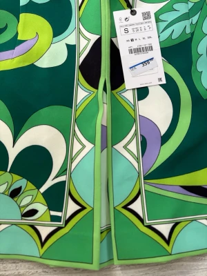 Grön mönstrad kortkjol från Zara - Säljer en färgstark kortkjol från Zara med grafiskt mönster i grönt, vitt, svart, lila och lime. Kjolen har en A-linjeform och är tillverkad i ett mjukt material som känns lyxigt. Perfekt för dig som vill sticka ut med coola retrovibbar.