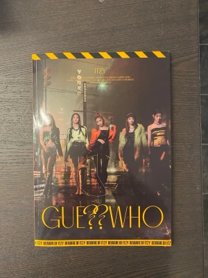 ITZY GUESS WHO album fotobok - Säljer en snygg fotobok från ITZYs album GUESS WHO. Omslaget har en mörk, urban känsla med gruppens medlemmar i coola outfits och gul text. Boken är tryckt på glansigt papper och har detaljer i svart och gult. Perfekt för K-pop fans!