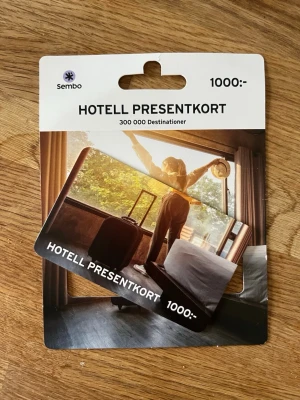 Hotell presentkort Sembo 1000 kr - Presentkort från Sembo på 1000 kr som gäller för hotellvistelser på över 300 000 destinationer. Kortet är svart med vit text och levereras i ett pappersfodral med bild på en person i hotellrum. Perfekt för dig som vill ge bort en resa eller hotellupplevelse.