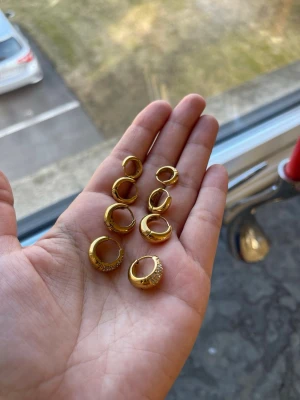 Guldpläterade chunky hoops örhängen - Säljer ett set med guldpläterade chunky hoops örhängen i olika storlekar. Några av örhängena är dekorerade med små gnistrande stenar för extra bling, medan andra har en slät, blank finish. Perfekta för att mixa och matcha till olika looks. Material hög kvalitet rostfritt stål, vattentåliga.