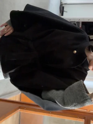 Poncho kappa - Svart poncho kappa med guldknapp och band från Nelly. Oanvänd med lapp kvar. Strl One Size så passar dem flesta. Perfekt vårjacka! 