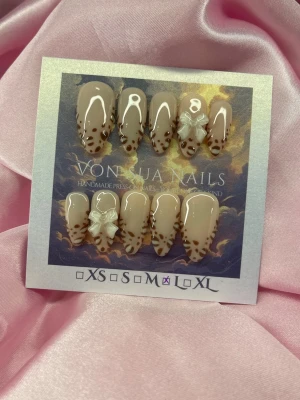 SoftLeo(L);Medium Almond - Snygga handgjorda press-on naglar i nude med brunt leopardmönster och vita 3D-rosetter. Naglarna har en medium längd och almondform med glansig finish. Perfekt för dig som vill ha en trendig och unik look.L: 17 mm, 12,5 mm, 13 mm, 12 mm, 10 mm 