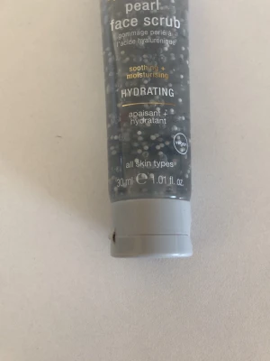 Pearl face scrub 30 ml vegansk - Hydrerande ansiktsskrubb med pärleffekt och hyaluronsyra. Passar alla hudtyper och är vegansk. Tuben är genomskinlig med vita pärlor och har grått lock. Perfekt för dig som vill ha en återfuktande och lugnande skrubb i smidig storlek.