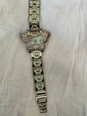 Silverfärgad klocka med fjäril och stenar - Unik klocka i silverfärg med fjärilsformad urtavla dekorerad med rosa och vita stenar. Armbandet har utskurna fjärilar och matchande detaljer. Perfekt för dig som gillar söta accessoarer med lite extra bling.250kr använder mig av Postnord,pm vid intresse 🩷