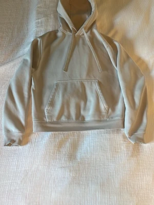 Zara hoodie - Snygg beige hoodie med klassisk huva och dragsnören. Hoodien har en stor magficka framtill och ribbade muddar vid ärmslut och nederkant. Perfekt för en avslappnad och stilren look. Materialet känns mjukt och bekvämt mot huden.