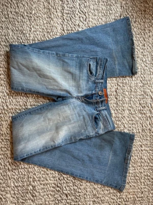 Blå bootcut jeans med slitningar - Säljer ett par ljusblå bootcut jeans med slitningar och snygg tvätt. Jeansen har råa kanter nedtill och dekorativa sömmar på bakfickorna. Klassisk denimlook i 100% bomull, perfekta till sneakers eller boots. Jag är 170 och de går ner till marken för mig! Köpta på londons second hand