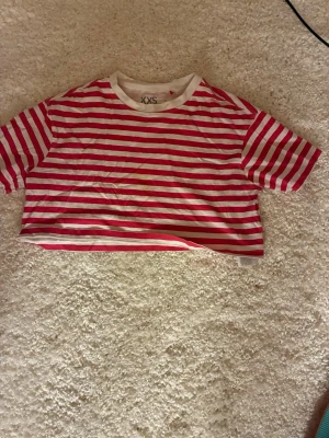 Rödvit randig crop t-shirt FSBN Sister - Säljer en kort röd och vit randig crop t-shirt från FSBN Sister. T-shirten har rund halsringning med vit kant och raka korta ärmar. Perfekt för en avslappnad och trendig look. Tillverkad i mjuk bomull för skön känsla.