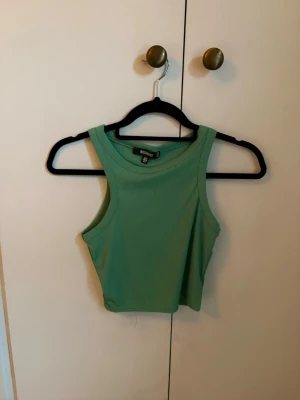 Grön ribbat linne - Snygg grön croppad linnetopp. Toppen är ribbad och ärmlös med en tight passform och breda axelband. Perfekt till sommaren och enkel att matcha med jeans eller kjol.