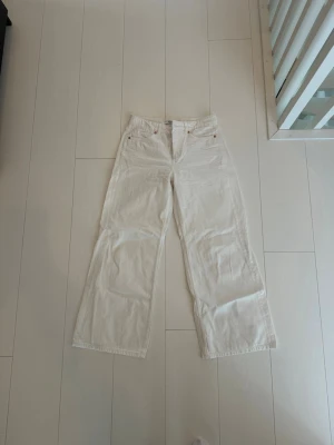 Vida vita jeans med hög midja - Säljer ett par vita jeans med hög midja och raka, vida ben. Klassisk femficksmodell med knapp och dragkedja fram. Perfekta till en avslappnad och trendig look. Materialet är kraftigt bomullstyg.