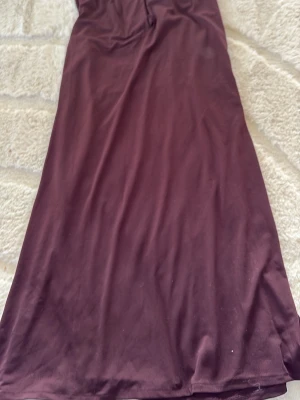 Vinröd långklänning med knytband - Säljer en vinröd långklänning i mjukt tyg med smalt knytband i midjan. Klänningen har en enkel, elegant siluett och passar perfekt för dig som gillar stilrena plagg. Inga synliga mönster eller detaljer förutom knytbandet.