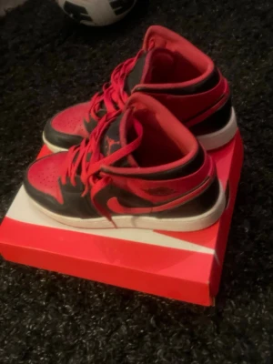 Nike Air Jordan 1 Low svart/röd - Säljer ett par Nike Air Jordan 1 Low sneakers i svart och rött med klassisk logga på sidan. Skorna har snörning, vit sula och är tillverkade i syntetmaterial och skinn. Perfekta för dig som vill ha en ikonisk och stilren sneaker med streetkänsla.