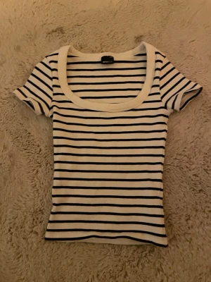 Randig topp från Gina Tricot - Säljer en vit och svart randig topp från Gina Tricot i storlek XXS. Toppen har korta ärmar, rundad djup ringning och är gjord i mjuk bomull. Perfekt för en enkel och stilren look.