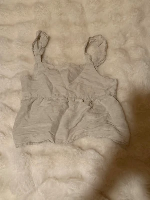 Ljusgrå/beige linnetopp från MANGO  - Säljer en ljusgrå/beige linnetopp från MANGO med axelband och lätt rynkad midja. Toppen har en avslappnad passform och är perfekt för varma dagar. Materialet känns mjukt och luftigt, och toppen har en enkel men söt design. Perfekt till sommaren. Passar xs