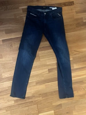 Mörkblå slim fit jeans från replay  - Snygga mörkblå slim fit jeans från replay med klassisk femficksdesign och diskreta slitningar. Jeansen har normal midja och smala ben, perfekta för en trendig och avslappnad stil. Tillverkade i stretchigt denim för extra komfort.
