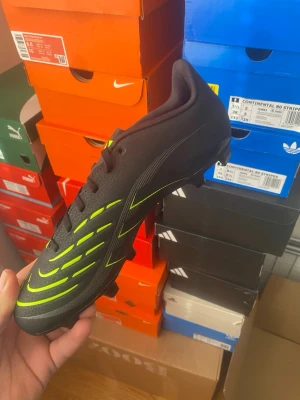 Adidas Predator Svart/Neongul Fotbollssko - Säljer en Adidas Predator fotbollssko i svart med neongula detaljer och klassiska ränder. Skon har snörning, låg profil och dobbar för spel på gräs. Tillverkad i syntetmaterial för bra grepp och kontroll på planen. Perfekt för dig som vill sticka ut på matchen.