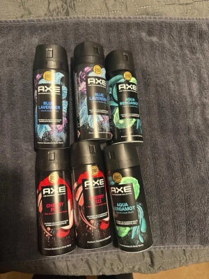 AXE Premium Fragrance Set 6 Bottles - Säljer ett 6-pack AXE deosprayer i dofterna Blue Lavender, Aqua Bergamot och Cherry Fizz. Flaskorna är svarta med färgglada detaljer i blått, grönt och rött. Perfekt för dig som vill ha variation bland dina dofter. Smidig sprayflaska i metall.