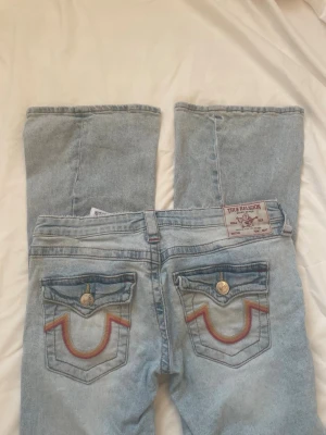 True Religion ljusblå bootcut jeans - Säljer ett par super snygga ljusblå bootcut jeans från True Religion med fina broderade fickor bak i rött och orange. Jeansen hade 1 hål som jag sydde ihop så det syns inte ens längre, har några små fläckar som ej syns vid användning. Nypris 1300. Inga andra defekter som jag märkt. De är i storlek 27. PRISET GÅR ATT DISKUTERAS🥹💗😛