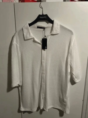 Vit skjorta i strukturerad bomull - Vit skjorta från  strukturerad bomull med klassisk krage och knappar framtill. Skjortan har trekvartsärm och en loose passform som ger en avslappnad vibe. Perfekt till sommarens alla looks.