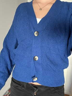 Blå ribbad kofta med stora knappar - Blå ribbad kofta med v-ringning och tre stora, ljusa knappar framtill. Koftan har lite oversized passform och är väldigt mjuk och gosig! Endast använd 1-2 gånger. Storlek xs-s