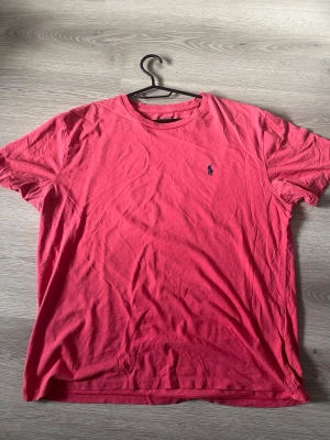 Röd t-shirt från Polo Ralph Lauren - Säljer en röd t-shirt från Polo Ralph Lauren med klassisk passform och rund hals. T-shirten har korta ärmar och den ikoniska lilla loggan broderad på bröstet. Tillverkad i mjuk bomull som är skön att bära hela dagen.