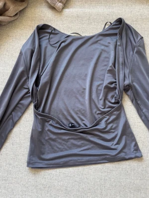 Topp med öppen rygg - Snygg grå topp med öppen rygg, lång ärm och lätt glansigt material, lite bikinimaterial tunt. Toppen  sitter figurnära. I storlek S från stradivarius.
