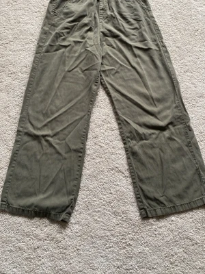 Olivgröna vida cargobyxor - Säljer ett par olivgröna cargobyxor med bred passform och raka ben är tillverkade i ett mjukt bomullstyg. Perfekta för en avslappnad och trendig look. Storlek170 motsvarar XS