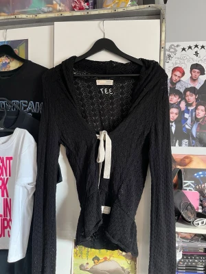 Svart kofta - Säljer en svart hoodie i spetsmaterial från odd molly. Tröjan har långa ärmar, luva  med ett vitt band framtill. Den har en figurnära passform och spetsdetaljer som ger en unik look.
