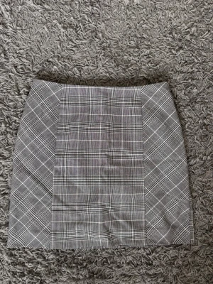 Grå rutig kort kjol minikjol storlek 36 - Snygg grå kortkjol med klassiskt rutigt mönster. Kjolen har en rak passform och är perfekt för att styla med en enkel topp eller oversized tröja. Materialet känns mjukt och följsamt, troligtvis i bomull eller polyesterblandning. Från H&M