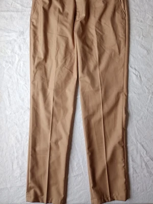 Beige kostym med kavaj och byxor - Säljer en stilren beige kostym med matchande kavaj och raka kostymbyxor. Kavajen har klassisk krage, två fickor med lock och en bröstficka. Byxorna har pressveck och sidfickor. Perfekt för dig som vill ha en clean och modern look.